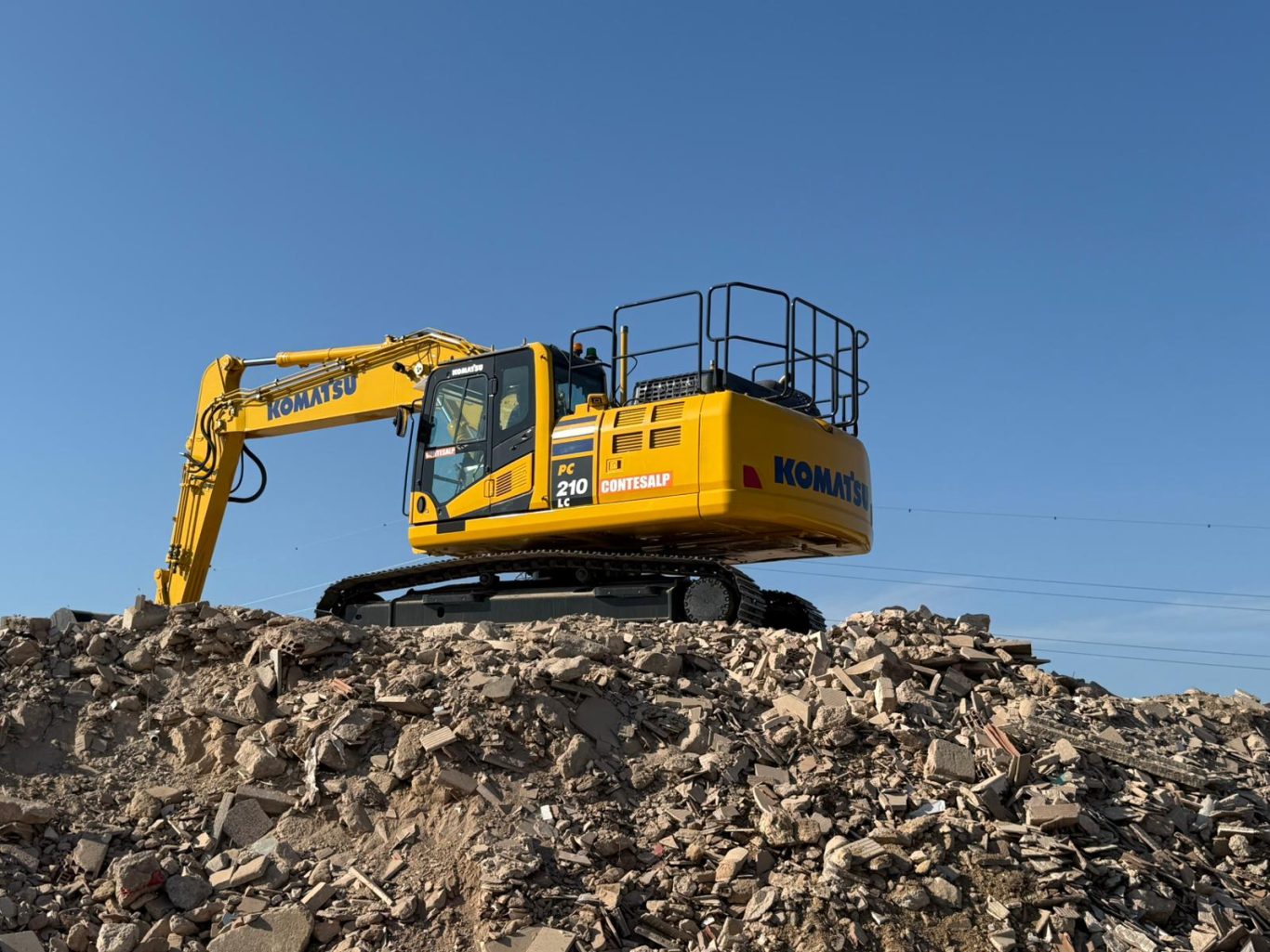 Pala cargadora con cadenas Komatsu LC210 Excavadora amarilla en una montaña de escombros bajo un cielo despejado.